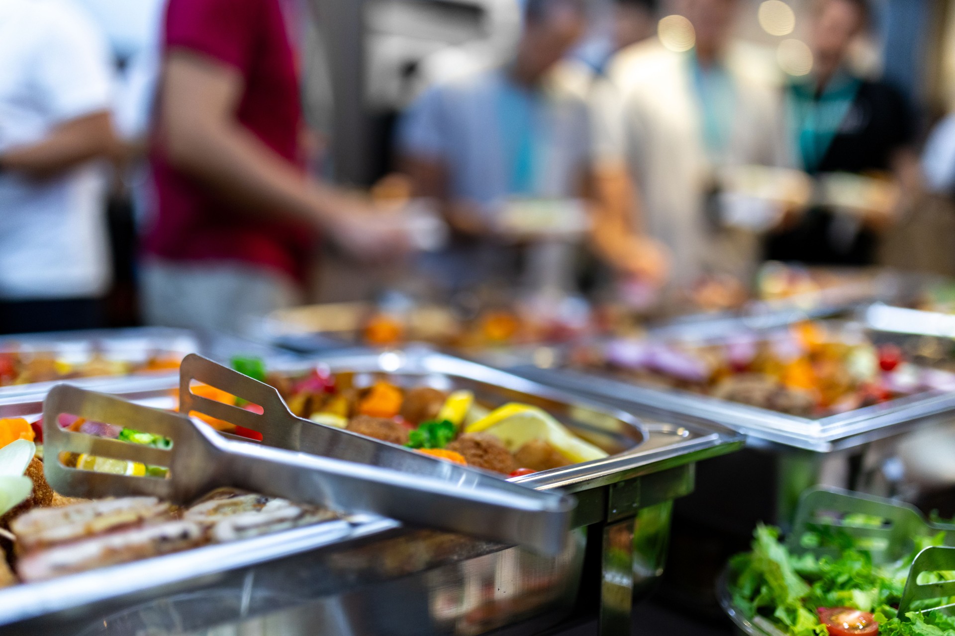 Buffet setup featuring a variety of colorful dishes and fresh salads at a crowded event in the afternoon