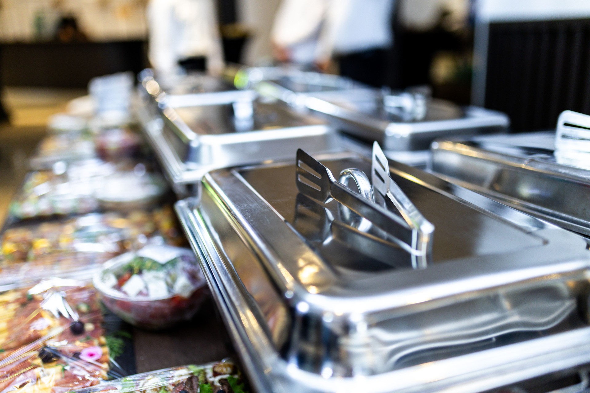 Catering buffet setup featuring silver serving trays and assorted dishes at a corporate event during evening hours